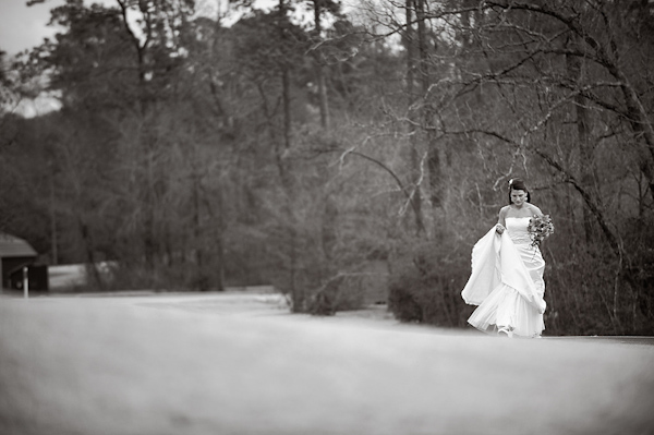 black and white photo - bride holding up dress as she walks through a field in the countryside - photo by Houston based wedding photographer Adam Nyholt